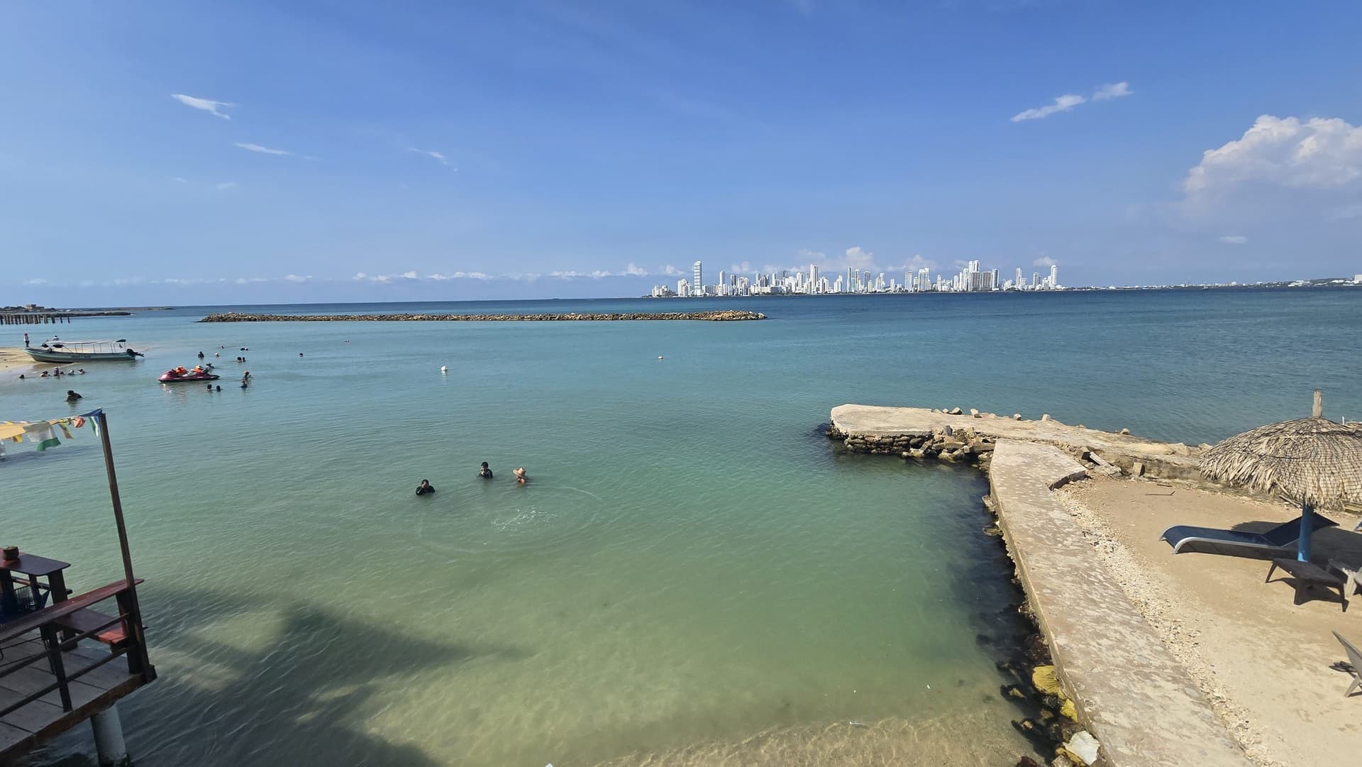Bahía de Paraíso del Sol en Tierra Bomba con el espolón de piedra, bañistas en el agua y el perfil de Cartagena al fondo.