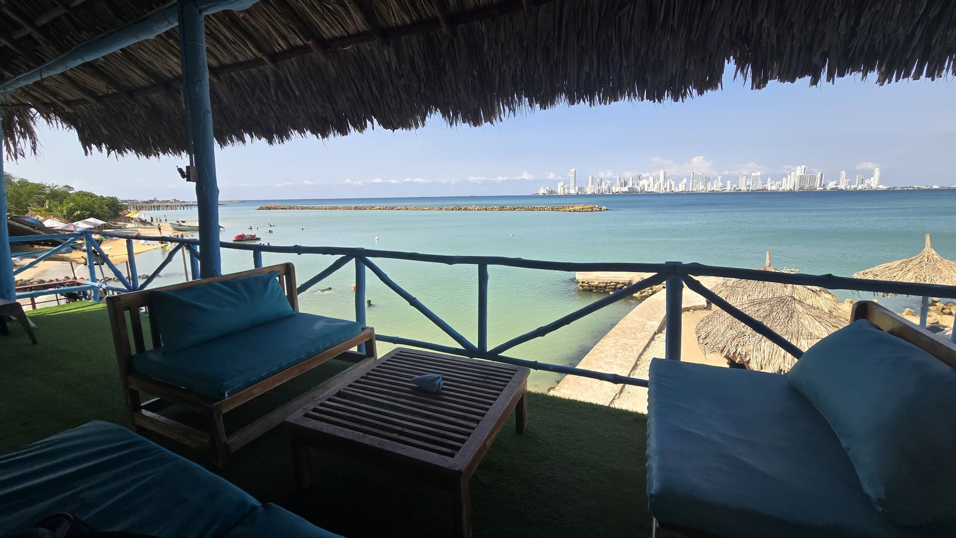 Mirador del segundo piso con techo de palma, sofás turquesa y vista a la bahía y a los edificios de Cartagena.